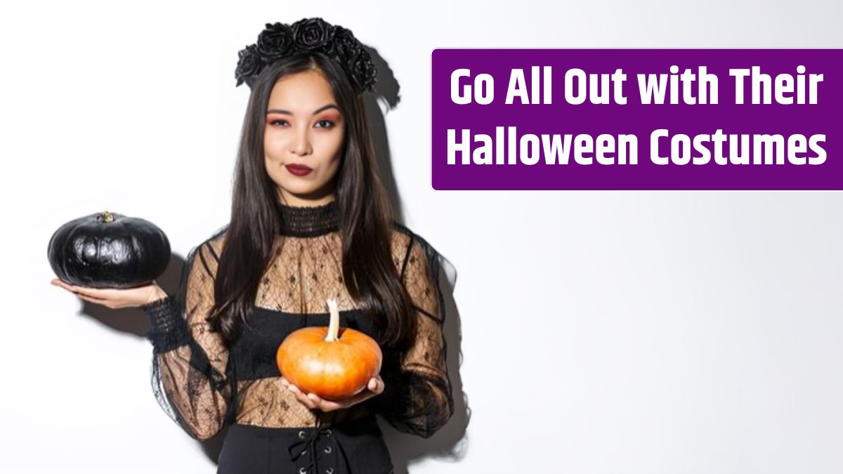 Sassy attractive asian girl in witch costume holding pumpkins and looking at camera standing.